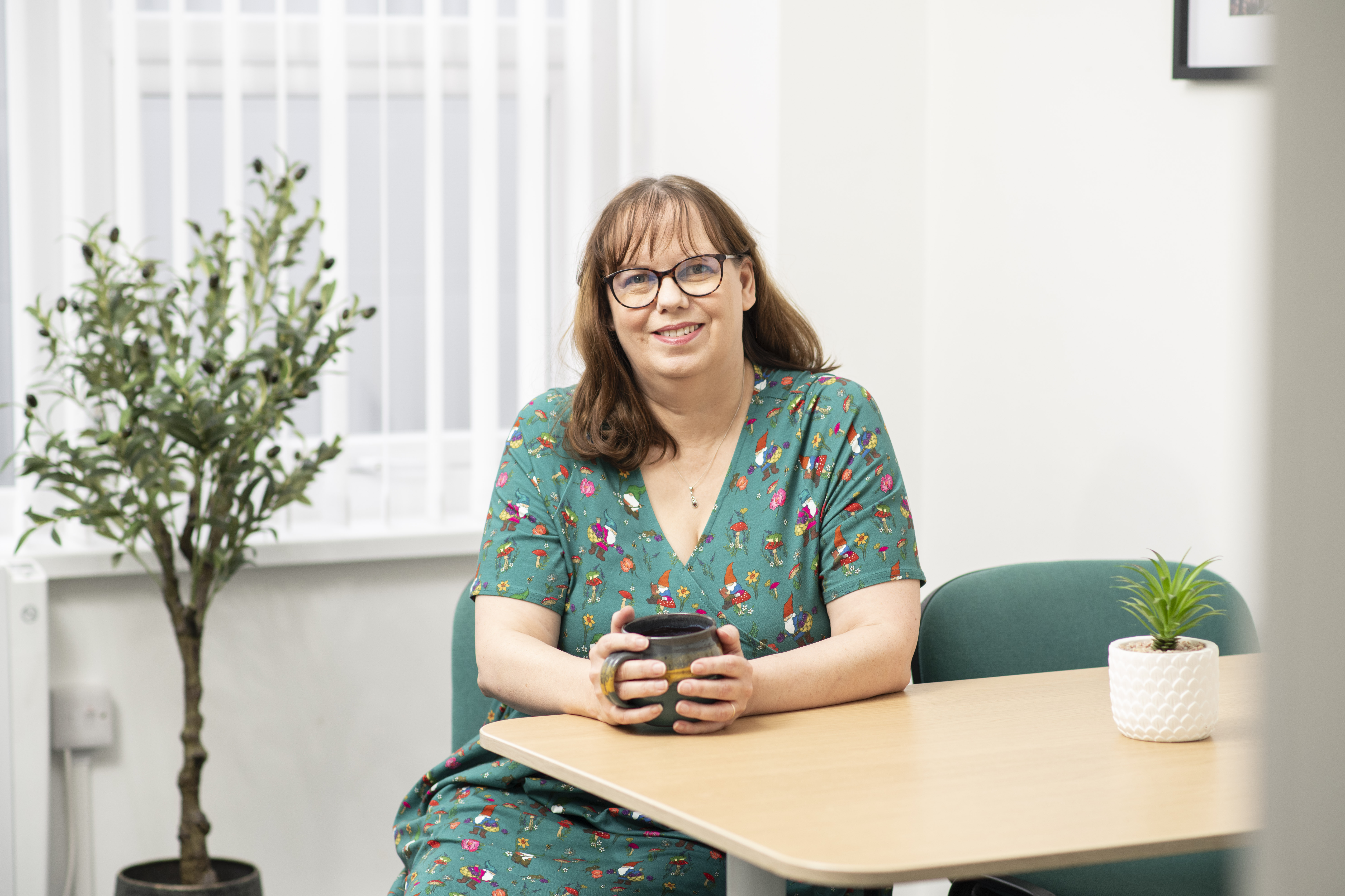 Photo of Kay wearing a green dress holding a cup of tea